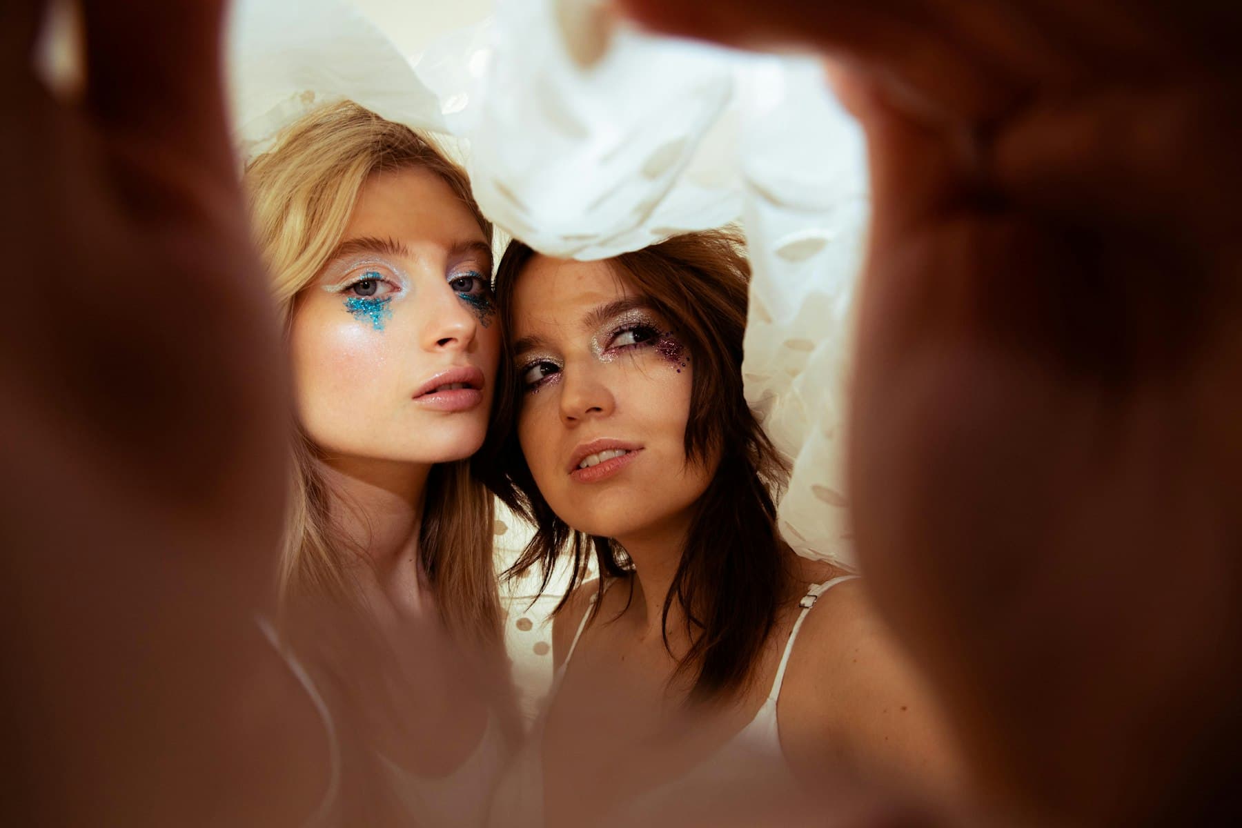 Two guests with glitter make-up framed by hands, close-up